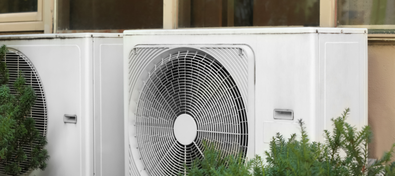 two outdoor hvac systems outside of a home next to some greenery