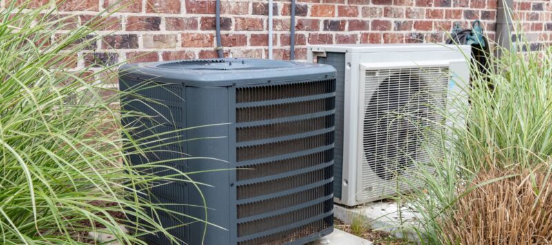 two outdoor hvac systems side by side next to a red brick home