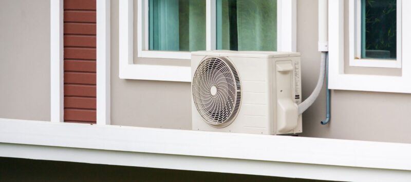 an outdoor air conditioner installed on the side of a home near the windows