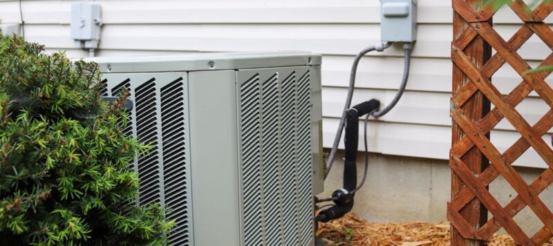 an outdoor ac unit next to a bush and a wooden fence