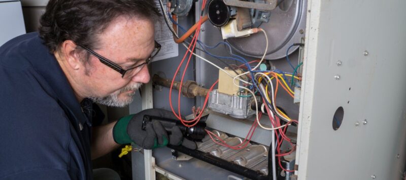 a heater technician using a flashlight to examine a unit