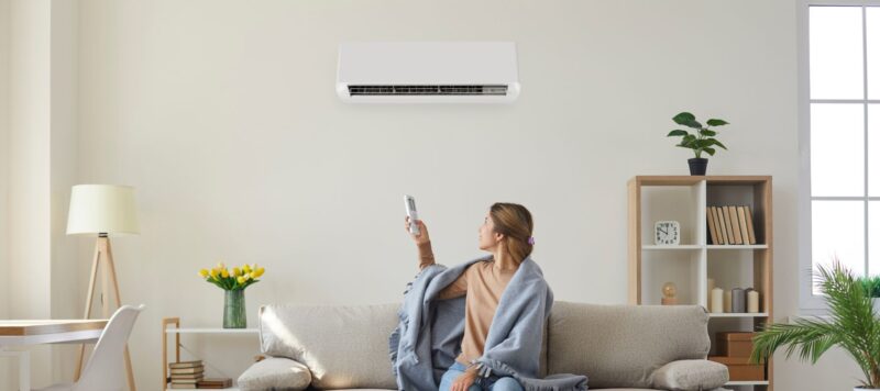 woman on a couch controlling her ductless ac with a remote